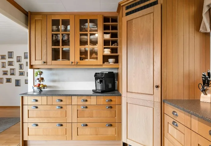 Cocina de madera de roble con armarios superiores acristalados, encimera oscura y cafetera en Burgos