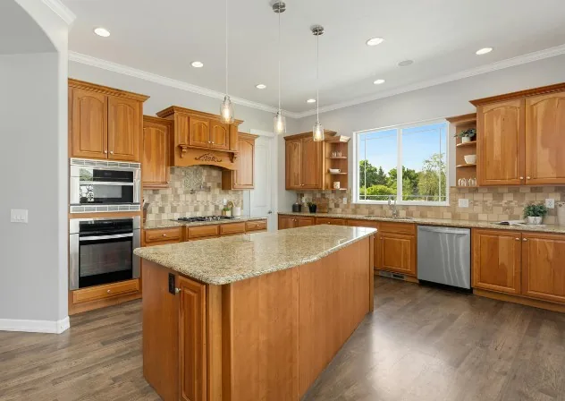 Cocina americana con isla central en madera color miel, encimera de granito y electrodomésticos de acero en Burgos