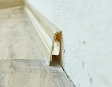 Primer plano de rodapié de madera clara recién colocado en encuentro con pared enfoscada en Burgos