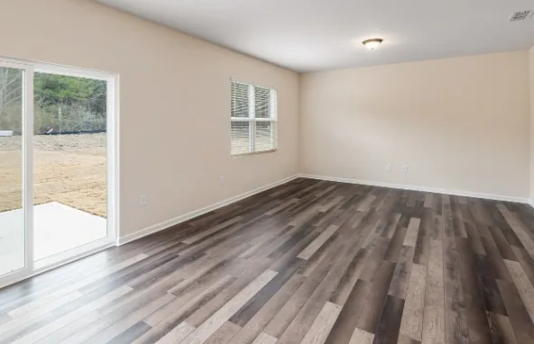 Salón vacío con suelo laminado gris oscuro, puerta corredera de cristal y ventana con persiana en Burgos