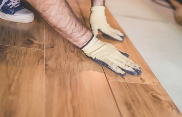 Operario con guantes instalando suelo laminado color miel, encajando una tabla a presión en Burgos