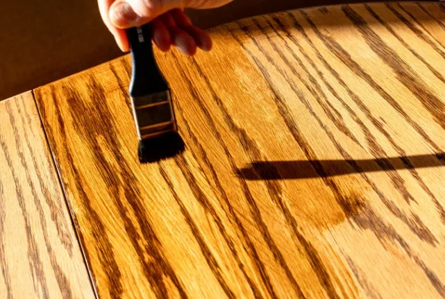 Mano barnizando con brocha una superficie de madera de roble con veta marcada en Burgos