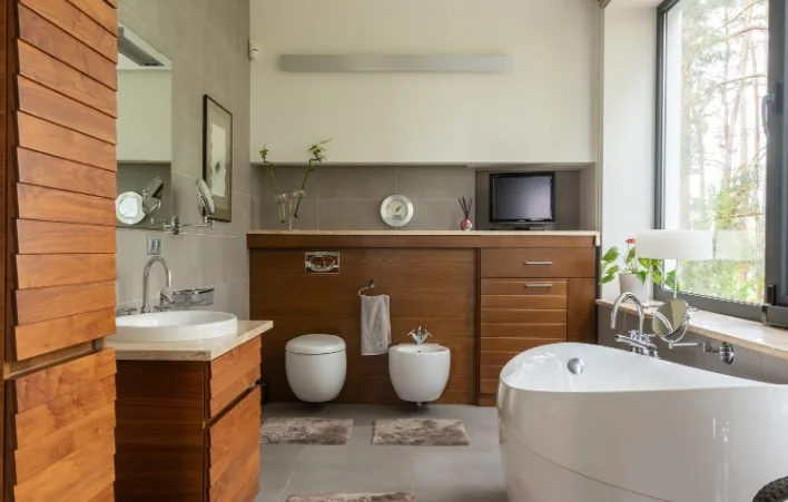 Baño con mueble bajo en madera de nogal oscuro, inodoro, bidé y bañera exenta junto a ventanal en Burgos