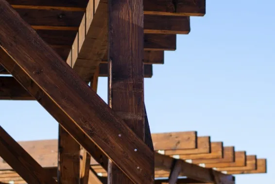 Primer plano de vigas de madera oscura tratada de una pérgola exterior contra cielo azul en Burgos