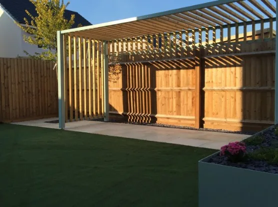 Pérgola moderna de lamas de madera clara con estructura metálica gris, junto a valla de madera en jardín en Burgos