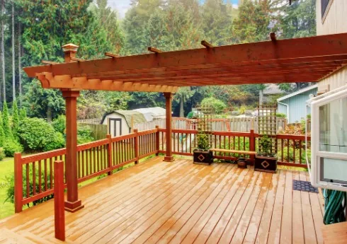 Terraza de madera con pérgola y barandilla en tono rojizo-caoba, jardín trasero con caseta al fondo en Burgos